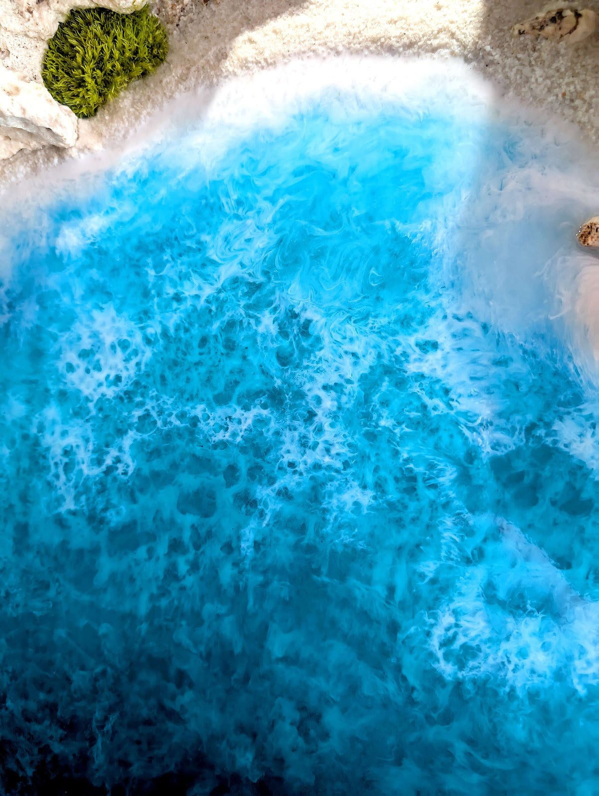 Aerial view of vibrant turquoise ocean water meeting sandy beach near greenery.