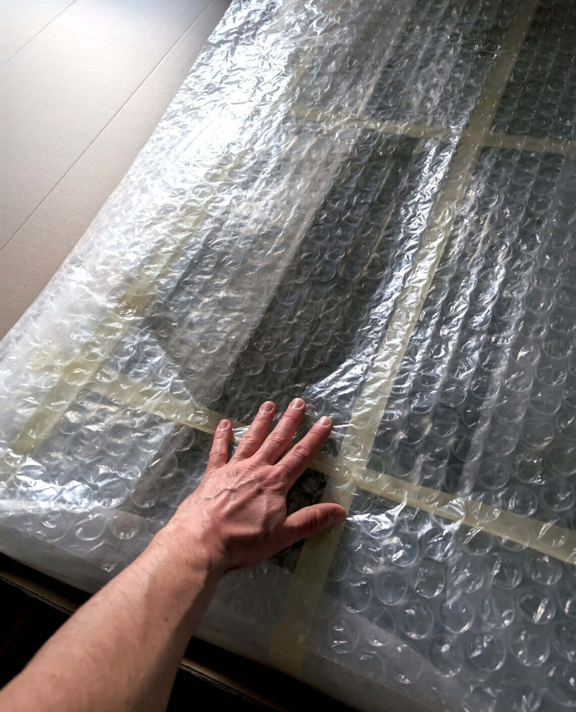 Hand touching bubble wrap on a large item, indicating careful handling and preparation for shipping.