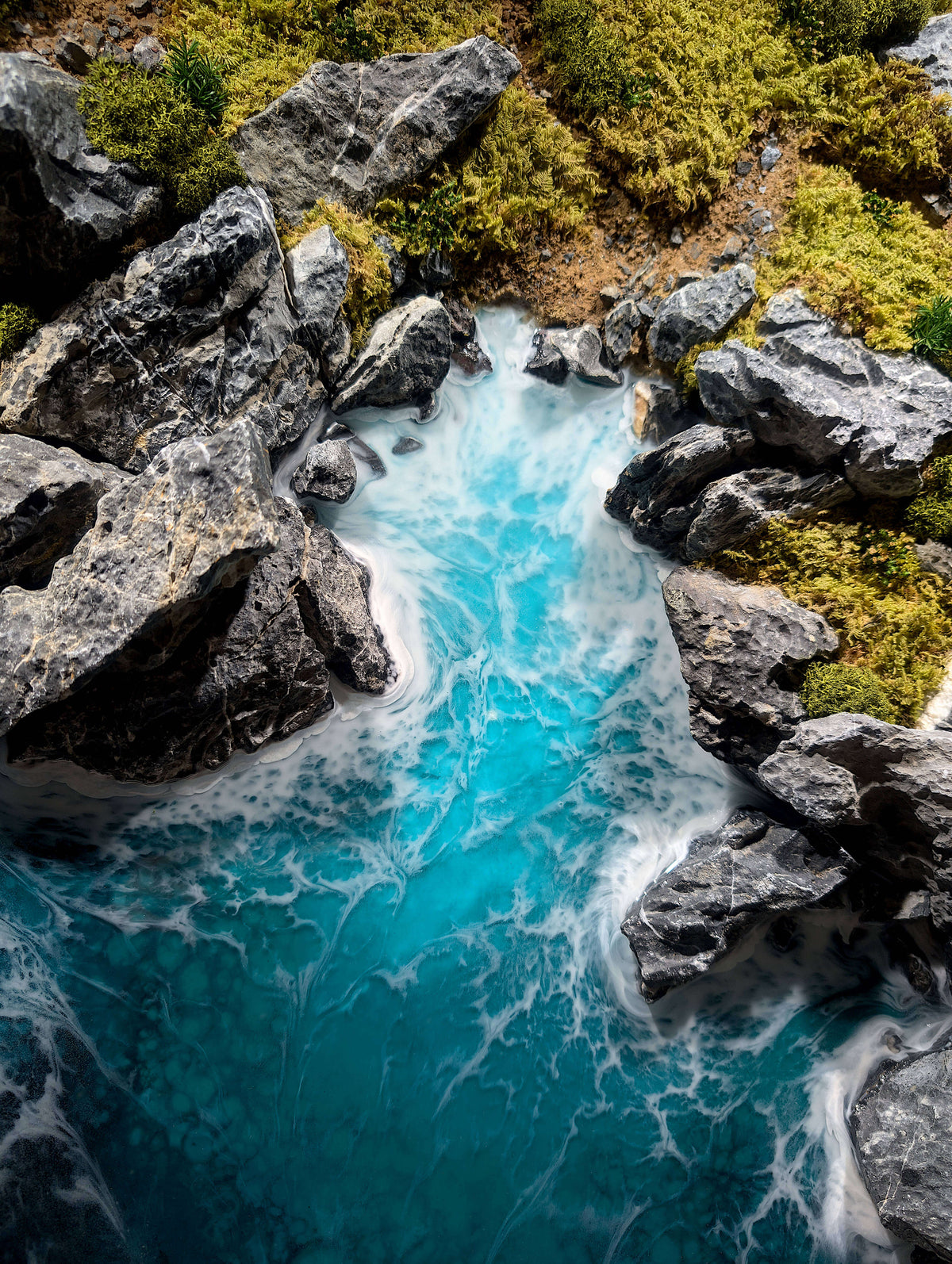 Above view of blue ocean water flowing between rocky shores with lush greenery in a diorama style.