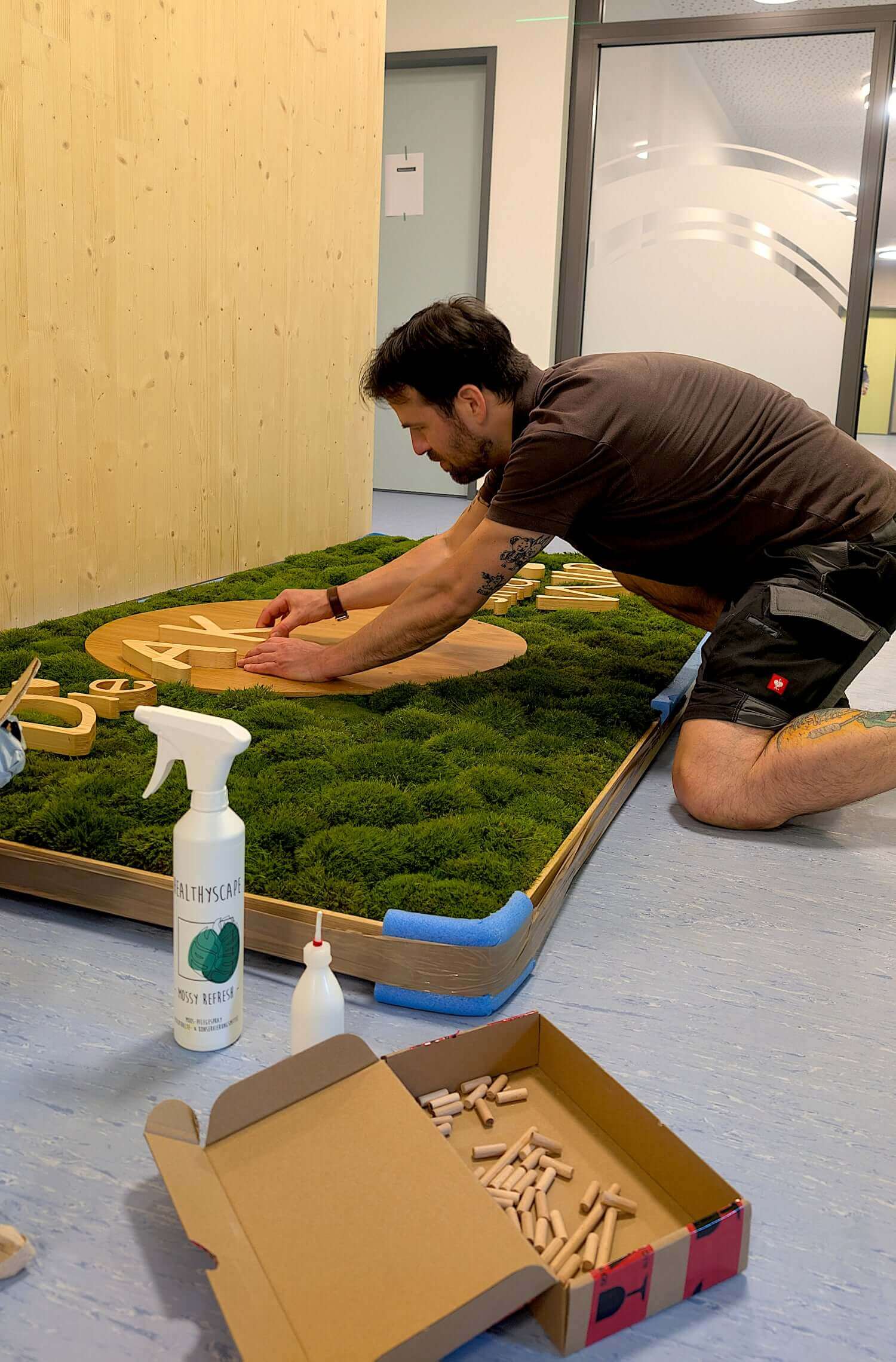 Ein Mann installiert ein Moosbild mit Holzlogo