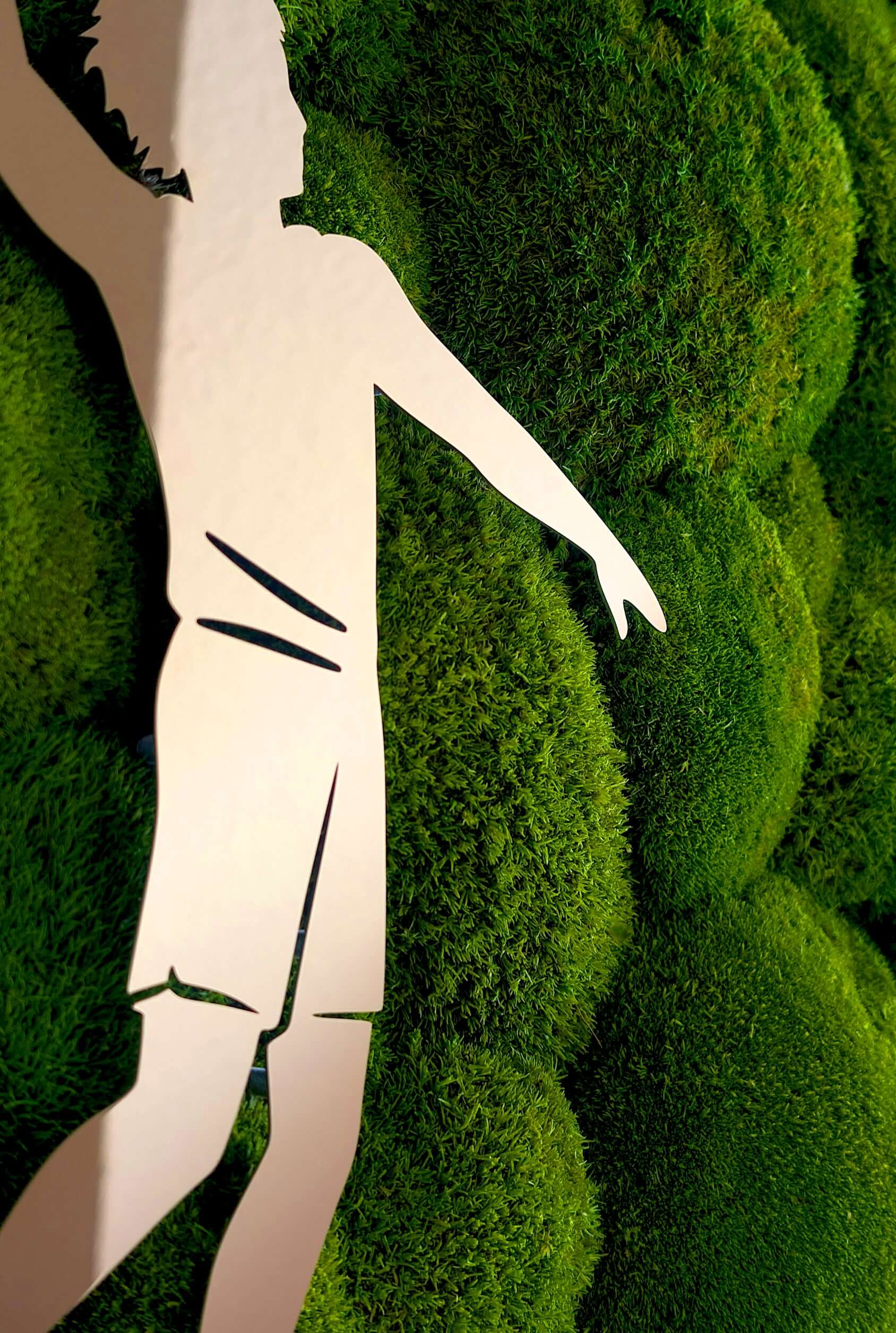 Moosbild mit Firmenlogo aus Metall, Silhouette eines Sportlers auf grünem Mooshintergrund.