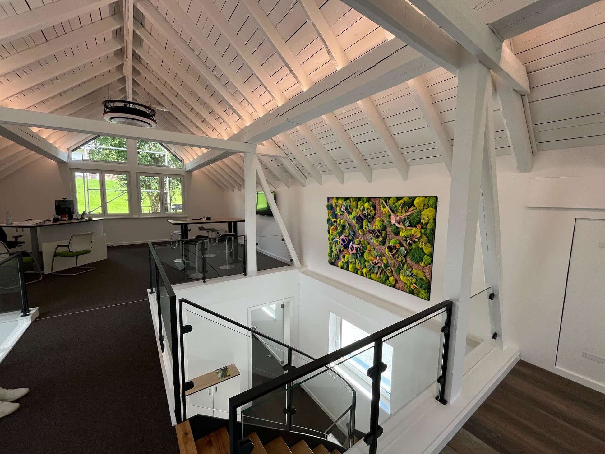 Modern workspace featuring a vibrant moss art piece 'Waldpfade Herbst' on the wall in a bright, airy loft.